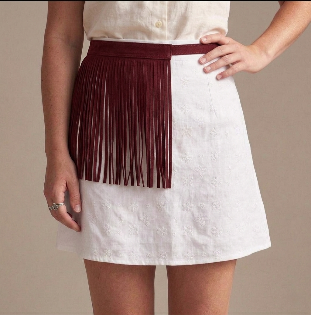 Cinturón de flecos burdeos de piel auténtica sobre falda blanca, estilo boho-chic italiano colección Riviera.
