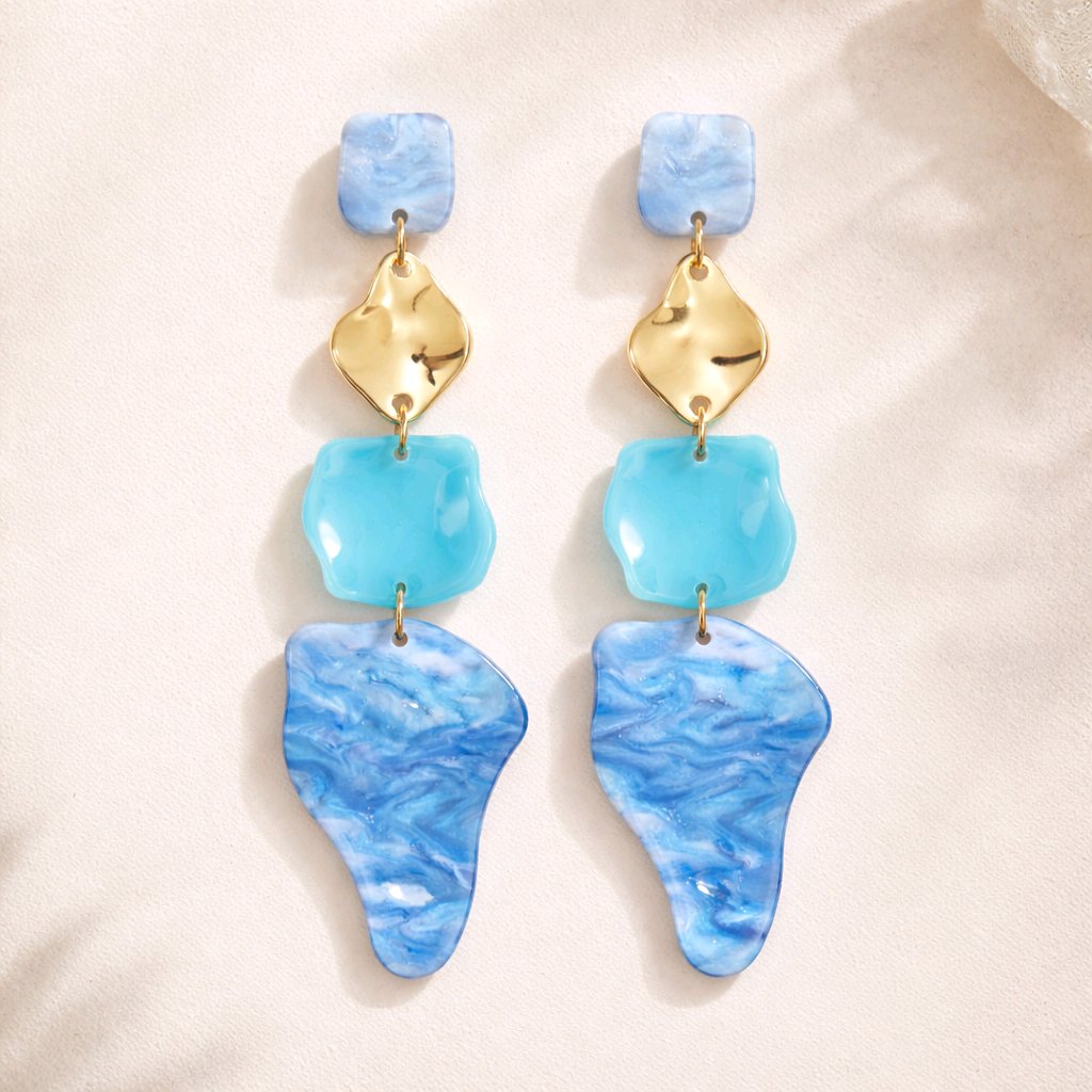 Pendientes colgantes asimétricos en acrílico azul océano y oro, bisutería de diseño escultórico ligera y sin níquel colección Riviera.
